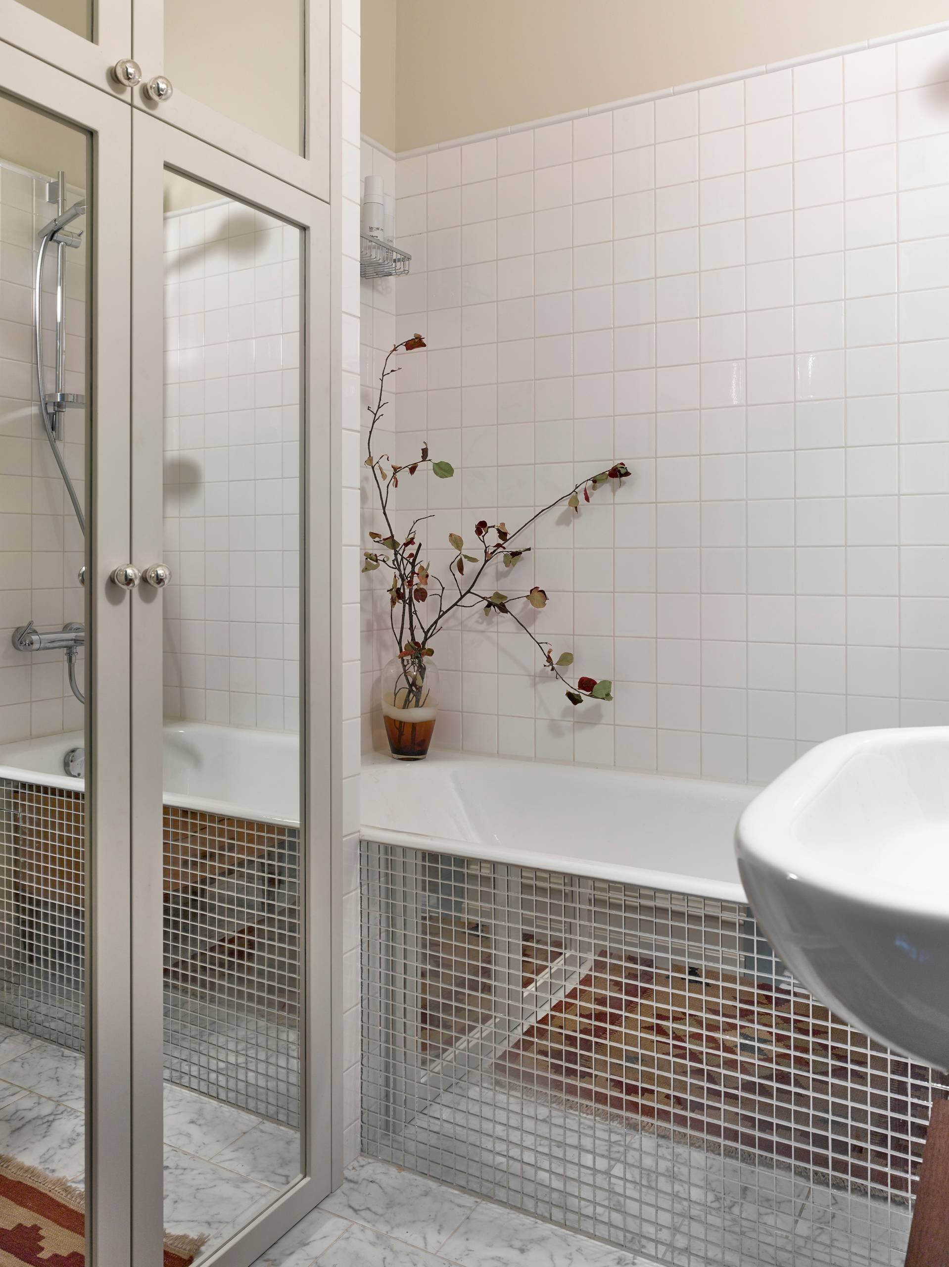 Ванная комната в современном стиле с ванной в нише, белой плиткой и бежевыми стенами. Высокий зеркальный шкаф